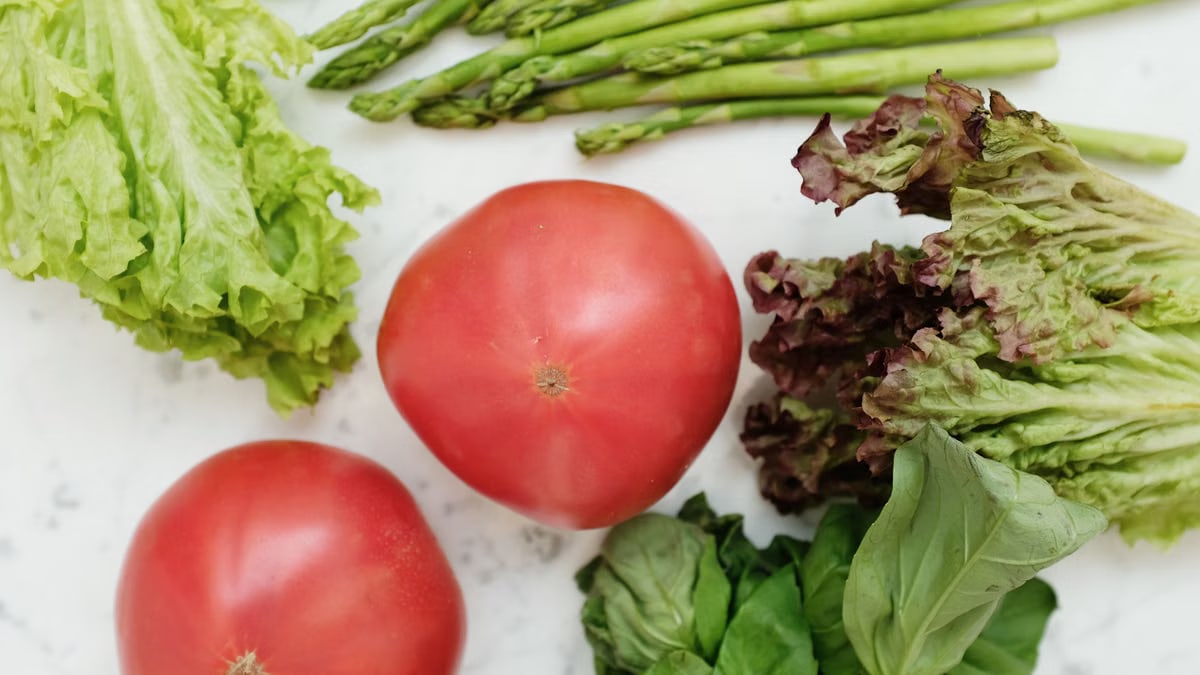 Close-up of fresh vegetables including lettuce, tomatoes, and asparagus for healthy cooking.